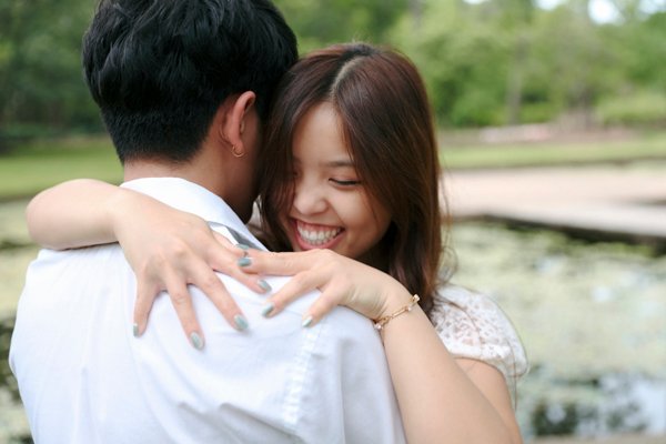 A joyful woman embracing her partner during a candid outdoor couple session, smiling brightly as she wraps her arms around him—captured by Photos by Gray in Katy, Texas.